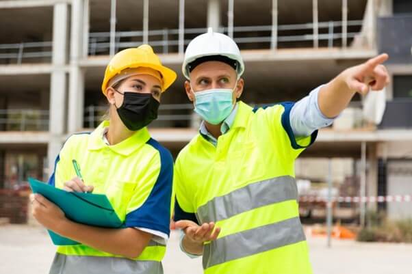 Un homme avec un casque pointe du doigt un chantier de construction.